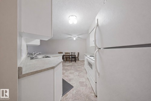 Kitchen featuring white cabinetry and appliances, a double basin stainless steel sink, and light-toned countertops - 103 12110 119 Ave, Edmonton, AB - Indoor Photo Showing Kitchen