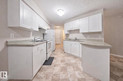 Kitchen featuring white cabinetry, light-toned countertops, and an integrated breakfast bar - 103 12110 119 Ave, Edmonton, AB - Indoor Photo Showing Kitchen With Double Sink