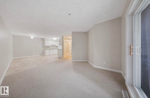 Spacious open-concept living area featuring light-toned carpeting and neutral wall colors - 103 12110 119 Ave, Edmonton, AB - Indoor Photo Showing Other Room