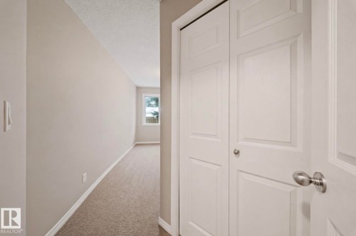 Hallway featuring neutral-toned walls, white baseboards, and textured carpeting - 103 12110 119 Ave, Edmonton, AB - Indoor Photo Showing Other Room