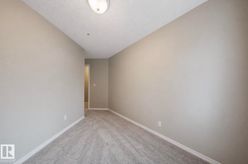 Interior room featuring neutral wall paint, carpet flooring, baseboard trim, and an overhead light fixture - 103 12110 119 Ave, Edmonton, AB - Indoor Photo Showing Other Room