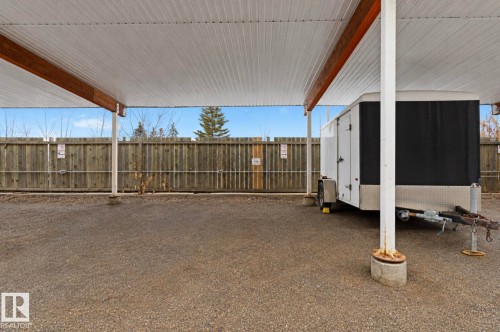 Covered gravel parking area featuring a corrugated metal roof and exposed wood beams, supported by white metal posts - 103 12110 119 Ave, Edmonton, AB -  With Exterior