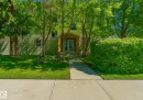 Entryway featuring a wood-clad portico with double glass doors, surrounded by mature trees, a manicured lawn, and lush green shrubbery - 103 12110 119 Ave, Edmonton, AB  - Outdoor 