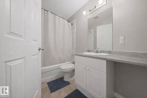 Bathroom featuring a white vanity with integrated sink, a spacious countertop, and a wall-mounted mirror with overhead lighting - 103 12110 119 Ave, Edmonton, AB - Indoor Photo Showing Bathroom