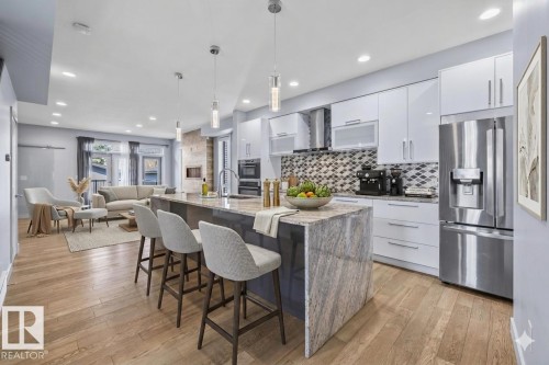 Spacious open-concept kitchen featuring an oversized island with waterfall edge, integrated stainless steel appliances, contemporary white cabinetry, and wood-finish flooring - 8706 88 Avenue, Edmonton, AB - Indoor Photo Showing Other Room