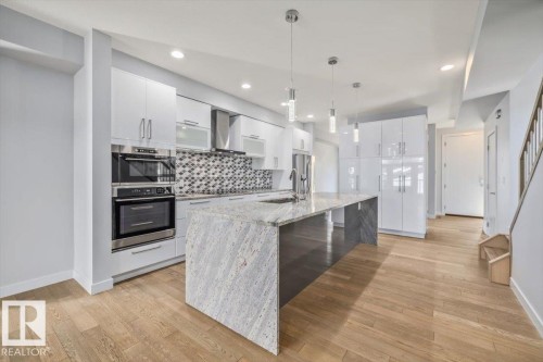 Kitchen featuring a large center island with a stone countertop, integrated sink, and modern pendant lighting - 8706 88 Avenue, Edmonton, AB - Indoor Photo Showing Kitchen With Upgraded Kitchen