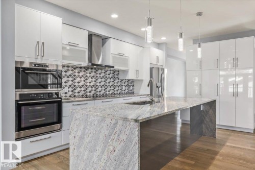 Gourmet kitchen featuring a large waterfall island with stone countertop, integrated sink, and pull-down faucet - 8706 88 Avenue, Edmonton, AB - Indoor Photo Showing Kitchen With Stainless Steel Kitchen With Upgraded Kitchen