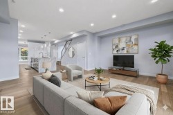 Open-concept living area featuring wood-finish flooring, recessed lighting, a modern staircase with dark railing, and a kitchen island with stone waterfall edge - 