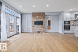 Open-concept living space featuring wood-finish flooring, a contemporary fireplace with a stone-clad surround, and recessed lighting - 
