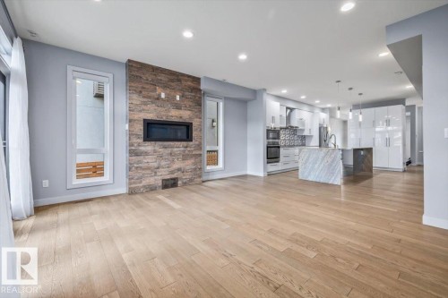 Open-concept living area featuring light wood-finish flooring, a built-in linear fireplace with a textured wood-look accent wall, and recessed lighting - 8706 88 Avenue, Edmonton, AB - Indoor Photo Showing Living Room With Fireplace
