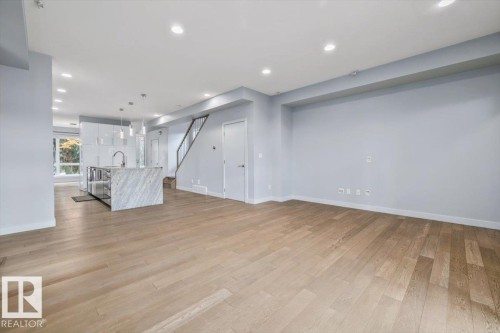 Open-concept living space with light wood-finish flooring, recessed ceiling lighting, and a kitchen island featuring a waterfall countertop - 8706 88 Avenue, Edmonton, AB - Indoor Photo Showing Other Room