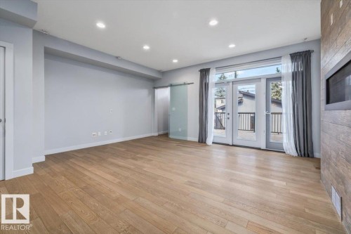 Spacious interior featuring wood-finish flooring, recessed lighting, and a barn door with frosted glass - 8706 88 Avenue, Edmonton, AB - Indoor Photo Showing Other Room