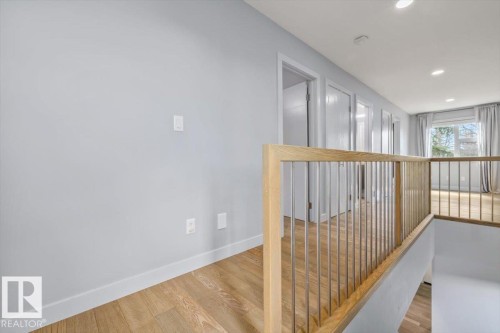 Light wood-finish flooring throughout, modern wood and metal railing, recessed lighting, and crisp white trim - 8706 88 Avenue, Edmonton, AB - Indoor Photo Showing Other Room