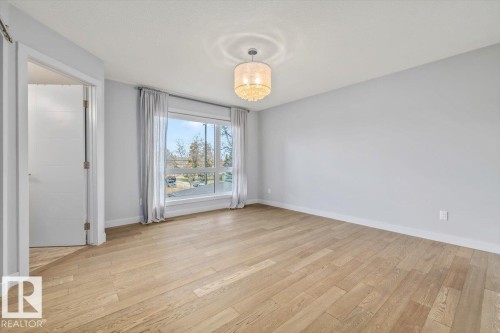 Spacious room featuring wood-finish flooring, a large window, a decorative ceiling light fixture, and a solid-core interior door - 8706 88 Avenue, Edmonton, AB - Indoor Photo Showing Other Room