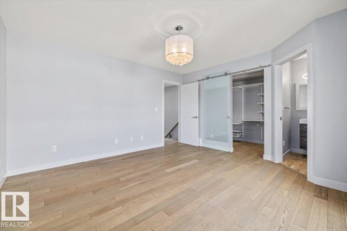 Light wood-finish flooring, a contemporary chandelier, a custom closet with built-in shelving, a frosted glass barn door, and a full bathroom with a single vanity - 8706 88 Avenue, Edmonton, AB - Indoor Photo Showing Other Room