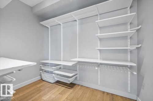 Customizable closet system with wood-finish flooring, white shelving, hanging storage, and pull-out storage bins - 8706 88 Avenue, Edmonton, AB - Indoor With Storage