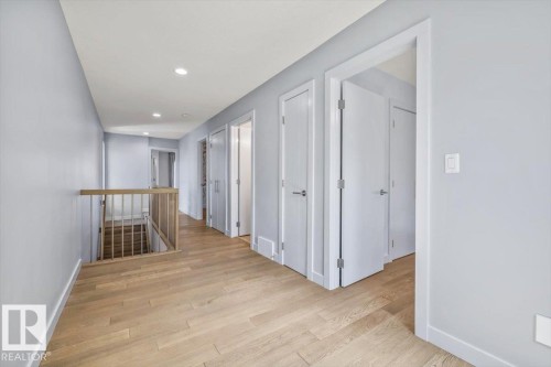Hallway featuring wood-finish flooring, recessed lighting, light gray wall paint, white trim, and a wood railing - 8706 88 Avenue, Edmonton, AB - Indoor Photo Showing Other Room