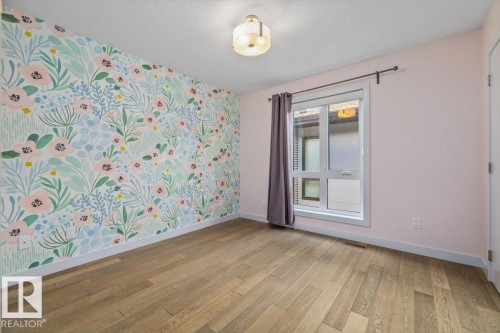 Room featuring wood-finish flooring, a decorative accent wall with floral pattern, and a single window with white trim - 8706 88 Avenue, Edmonton, AB - Indoor Photo Showing Other Room