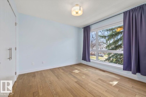 Bright room featuring wood-finish flooring, a large multi-pane window, white trim, a flush-mount ceiling light fixture, and a white interior door with brushed metal hardware - 8706 88 Avenue, Edmonton, AB - Indoor Photo Showing Other Room