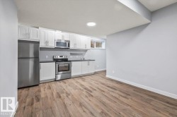 Kitchenette featuring stainless steel appliances, white cabinetry, dark countertops, and wood-finish flooring - 