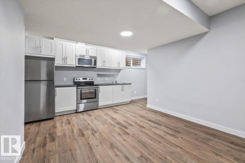 Kitchenette featuring stainless steel appliances, white cabinetry, dark countertops, and wood-finish flooring - 8706 88 Avenue, Edmonton, AB - Indoor Photo Showing Kitchen With Stainless Steel Kitchen