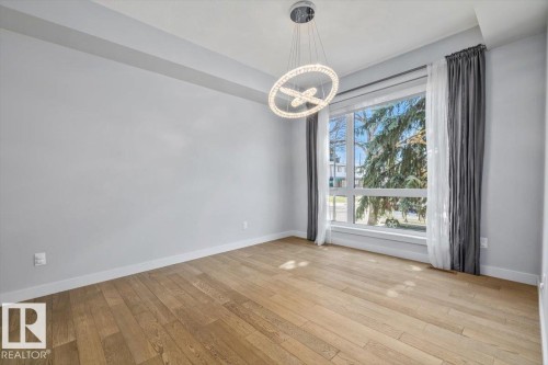 Spacious room featuring wood-finish flooring, a large multi-pane window, and a contemporary chandelier - 8706 88 Avenue, Edmonton, AB - Indoor Photo Showing Other Room