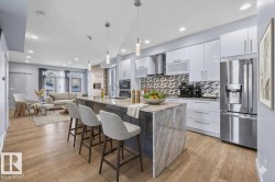 Spacious open-concept kitchen featuring an oversized island with waterfall edge, integrated stainless steel appliances, contemporary white cabinetry, and wood-finish flooring - 