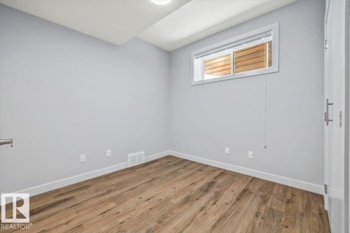 Spacious room featuring wood-finish flooring, light grey painted walls, white baseboards, and a white window frame - 8706 88 Avenue, Edmonton, AB - Indoor Photo Showing Other Room