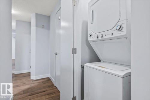 Vertical-stacked laundry appliances, wood-finish flooring, white baseboards, light-toned walls, and white interior doors - 8706 88 Avenue, Edmonton, AB - Indoor Photo Showing Laundry Room