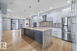Open-concept kitchen and living area featuring wood-finish flooring, a large island with a stone countertop, white cabinetry, and stainless steel appliances - 