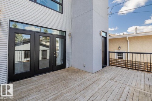 Expansive outdoor deck featuring wood-finish flooring, black metal railings, and dual exterior sconce lighting - 8706 88 Avenue, Edmonton, AB - Outdoor With Deck Patio Veranda With Exterior