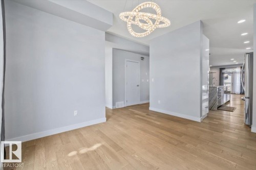 Expansive wood-finish flooring extends throughout the space, complemented by a contemporary chandelier light fixture - 8706 88 Avenue, Edmonton, AB - Indoor Photo Showing Other Room