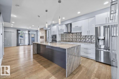 Open-concept kitchen and living area featuring wood-finish flooring, a large island with a stone countertop, white cabinetry, and stainless steel appliances - 8706 88 Avenue, Edmonton, AB - Indoor Photo Showing Kitchen With Stainless Steel Kitchen With Upgraded Kitchen