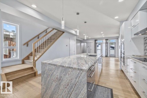 Contemporary kitchen featuring a large island with an integrated sink and pendant lighting, light wood-finish flooring, white cabinetry, a tiled backsplash, and recessed lighting - 8706 88 Avenue, Edmonton, AB - Indoor Photo Showing Kitchen With Upgraded Kitchen