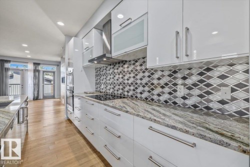 Modern kitchen featuring white high-gloss cabinetry, granite countertops, a mosaic tile backsplash, and a built-in cooktop with an overhead range hood - 8706 88 Avenue, Edmonton, AB - Indoor Photo Showing Kitchen With Upgraded Kitchen