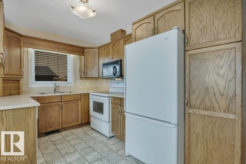 Kitchen featuring wood-finish cabinetry, a window over the sink, and white appliances including a refrigerator, range, and built-in microwave - 18227 76 Avenue, Edmonton, AB - Indoor Photo Showing Kitchen With Double Sink