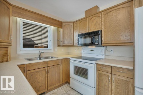 Kitchen featuring light wood-finish cabinetry, white countertops, dual stainless steel sink, black microwave, and white electric range - 18227 76 Avenue, Edmonton, AB - Indoor Photo Showing Kitchen With Double Sink