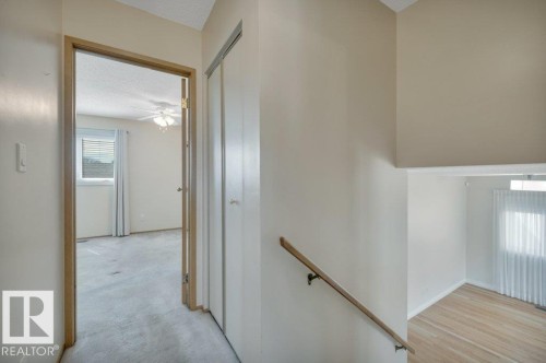 Interior hallway featuring light-toned walls, a wood handrail, and bi-fold closet doors - 18227 76 Avenue, Edmonton, AB - Indoor Photo Showing Other Room