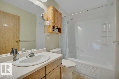 Bathroom featuring a white vanity with integrated sink, oak-finish cabinetry, a full-width mirror, and a white bathtub with a shower surround - 18227 76 Avenue, Edmonton, AB - Indoor Photo Showing Bathroom
