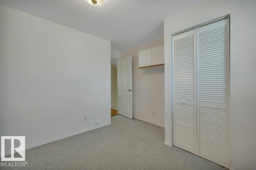 Carpeted room featuring a ceiling-mounted light fixture, white bi-fold louvered closet doors, and recessed overhead cabinetry with a wood-finish shelf - 18227 76 Avenue, Edmonton, AB - Indoor Photo Showing Other Room