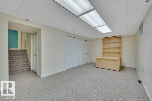 Finished lower level featuring neutral carpeting throughout, a drop ceiling with integrated fluorescent lighting, and a built-in wooden desk with shelving - 18227 76 Avenue, Edmonton, AB - Indoor Photo Showing Other Room
