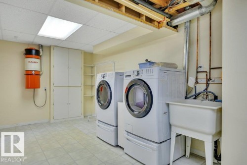 Dedicated laundry area featuring ceramic tile flooring, built-in storage cabinetry, open shelving, a utility sink, and a central vacuum system - 18227 76 Avenue, Edmonton, AB - Indoor Photo Showing Laundry Room