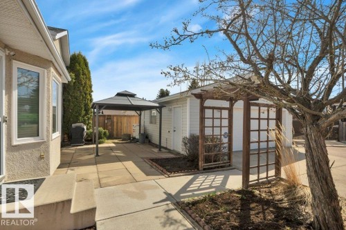 Spacious paved patio area featuring a detached garage, a wooden trellis, and mature landscaping - 18227 76 Avenue, Edmonton, AB - Outdoor