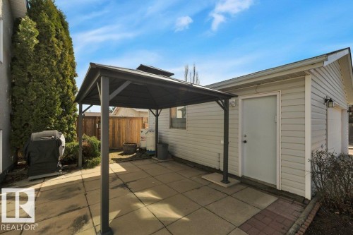 Paved patio area featuring a dark-framed gazebo, durable siding exterior, brick-edged pathway, and mature evergreen privacy trees - 18227 76 Avenue, Edmonton, AB - Outdoor With Exterior