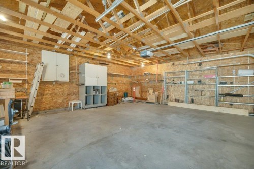Spacious garage featuring a concrete floor, exposed wood ceiling trusses, and organized wall-mounted shelving systems - 18227 76 Avenue, Edmonton, AB - Indoor Photo Showing Garage