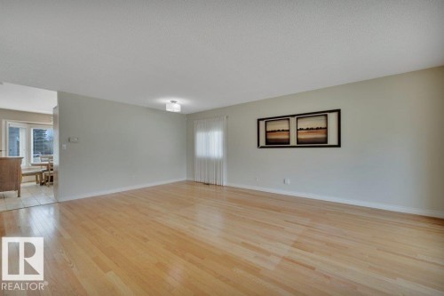 Spacious living area featuring light wood-finish flooring, neutral wall tones, and a semi-flush mount ceiling light fixture - 18227 76 Avenue, Edmonton, AB - Indoor