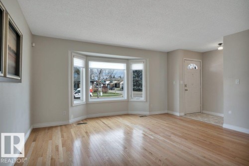 Spacious room featuring light wood-finish flooring, a prominent bay window with roller blinds, and neutral wall paint - 18227 76 Avenue, Edmonton, AB - Indoor