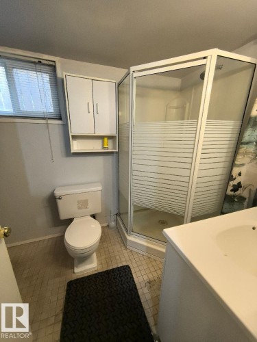 Compact bathroom featuring a corner shower enclosure with frosted privacy panels, a white toilet, and a white wall-mounted storage cabinet - 10815 68 Avenue, Edmonton, AB - Indoor Photo Showing Bathroom