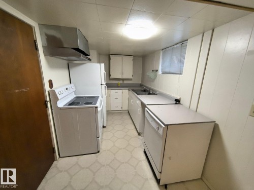 Kitchen featuring white cabinetry, a double basin sink, white freestanding range, stainless steel range hood, and white refrigerator - 10815 68 Avenue, Edmonton, AB - Indoor Photo Showing Laundry Room