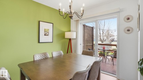 Dining area featuring a wood-finish table, an overhead chandelier, and a sliding glass door leading to an outdoor deck - 80 287 Macewan Road, Edmonton, AB - Indoor Photo Showing Dining Room